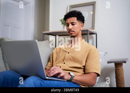 Man Sitting on a Sofa Using a Laptop in a Comfortable Home Environment Stock Photo