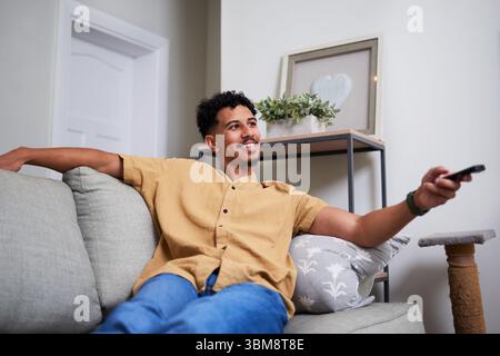 Relaxed Man Sitting on Couch Holding TV Remote and Smiling in Comfortable Home Setting Stock Photo