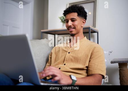 Young Man Smiling While Using a Laptop at Home in Relaxed Setting Stock Photo