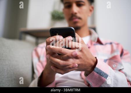 Young Individual Using Smartphone While Relaxing Indoors at Home on a Comfortable Couch Stock Photo