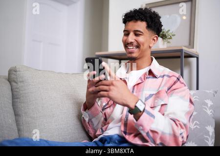 Smiling Man Relaxing at Home While Using Smartphone on Couch Stock Photo