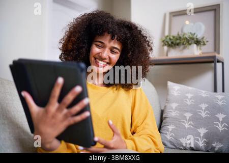 Young Woman Smiling While Using a Tablet in a Cozy Home Setting Stock Photo