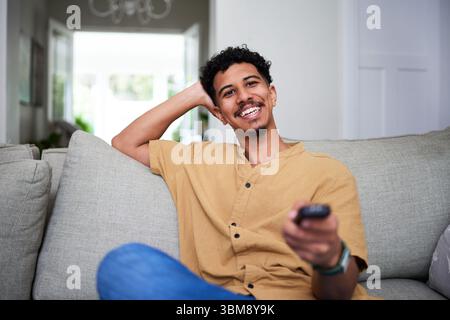 Relaxed Young Man Smiling and Watching Television in a Cozy Home Setting Stock Photo