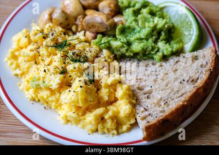 London UK June 25 2025,  Scambled Eggs With Mashed Avacado Fried Musherooms and Seeded Bread Stock Photo