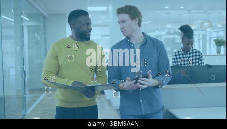 Two male colleagues examining document folder and discussing in modern office, with glass partition. Collaboration, professionalism, modernity, teamwo Stock Photo