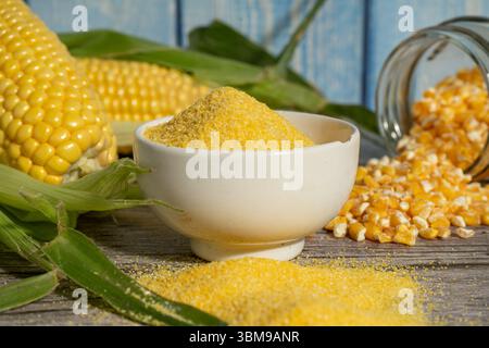 Corn flour or polenta in a bowl with fresh corn cobs and corn grits on rustic wooden table Stock Photo