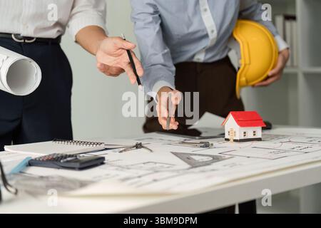 Project Collaboration and Architectural Planning. Professionals strategizing over architectural designs with tools and a model house. Stock Photo