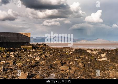 A rocky beach with a large rock wall in the background. The sky is cloudy and the beach is empty Stock Photo
