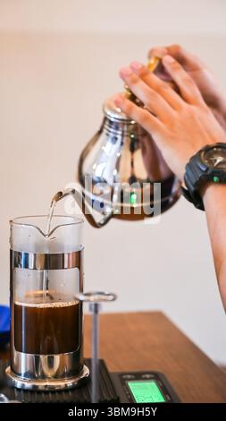 Barista making filter coffee, pouring hot water from kettle into french press coffee maker Stock Photo
