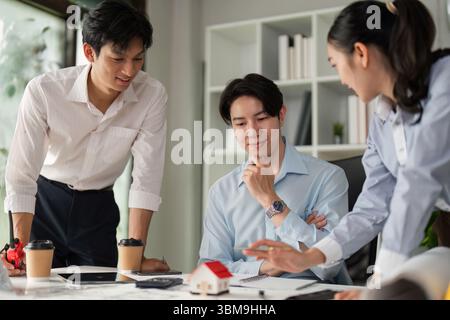 Design Presentation and Collaboration. A professional team discussing a model house design with blueprints on the table. Stock Photo