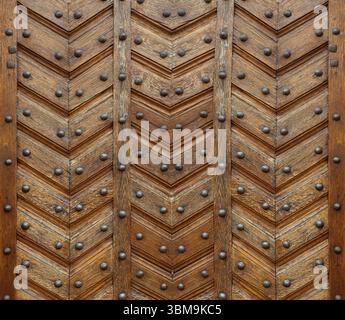 Antique wooden door with chevron pattern and rivets, creating a textured background with historical charm Stock Photo