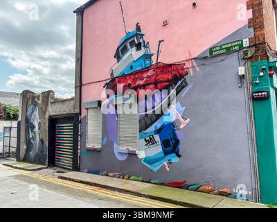 Large boat mural painted on the side of a building in Dublin, Ireland. Street art depicting a colorful boat, with another portrait mural nearby. Stock Photo