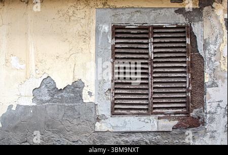 Rusty metal ventilation window on a decaying exterior wall with damaged plaster, showing time and weather damage Stock Photo
