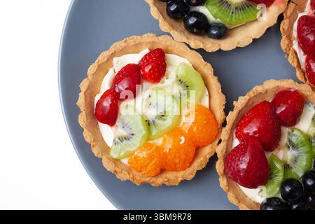 Pastry tarts with fresh fruits. Colorful mini cakes with kiwi strawberry orange and grape. Sweet dessert on blue plate. Natural ingredients. Stock Photo