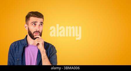 Portrait of pensive young bearded man touching his chin, deep in Stock Photo