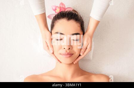 Young asian woman enjoying skin lifting face massage at wellness center Stock Photo