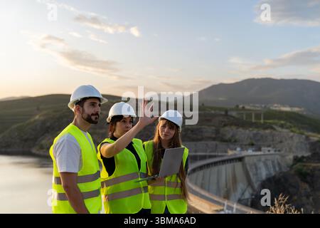Engineers using laptop discussing project near dam at sunset Stock Photo