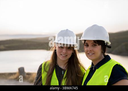 Female engineers wearing hard hats and safety vest smiling at construction site Stock Photo