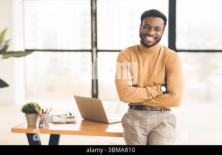 Successful black man sitting on desk at office Stock Photo