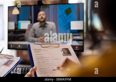 Closeup of cv resume of female job candidate being help by a person during a meeting with remote manager. Selective focus of a curriculum vitae in the hands of an individual attending a video call. Stock Photo