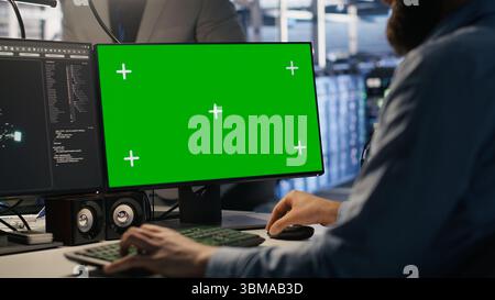 Engineer using green screen mockup PC in data center to update servers tech, configuring equipment using software tools. Server room worker reviewing hardware analytics on chroma key PC, camera A Stock Photo