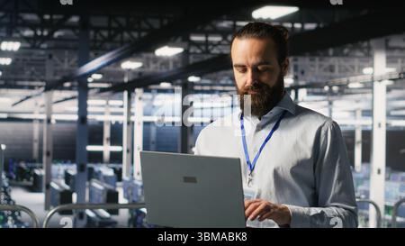 Computer scientists on data center industrial platform analyzing performance outputs on laptop. Server farm IT experts collaborating on finetuning rigs configurations Stock Photo