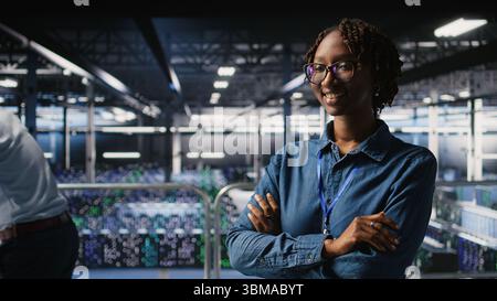 Happy technician next to server hub engineering team colleagues reviews AI diagnostics. Cheerful african american woman working in data center to maintain operational reliability, Stock Photo