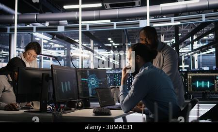 Data center engineers use laptop, collaborating on doing AI software updates. Server room teamworking colleagues doing brainstorming, optimizing infrastructure using artificial intelligence, camera A Stock Photo