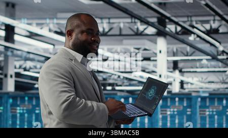 Smiling data center technician installing and upgrading hardware components. Happy server farm employee doing job tasks, implementing backup solutions to protect against data loss, camera B Stock Photo