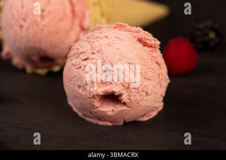 melting ice cream on a black slate board, sweet cold pink ice cream with strawberry flavor, ice cream in a waffle cone Stock Photo