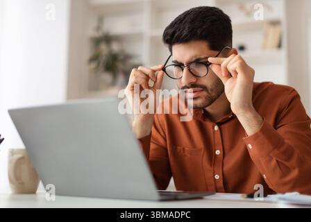 Confused Arab guy using laptop looking at screen Stock Photo