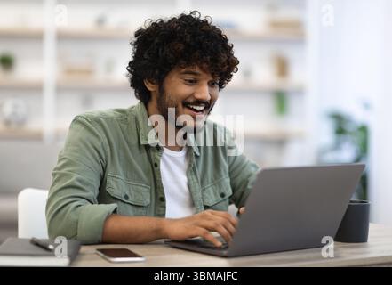 Happy dark-skinned young man using modern laptop Stock Photo