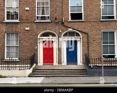 Two classic red and blue doors side-by-side on a brick building facade in Dublin, Ireland. Features steps and windows. Stock Photo
