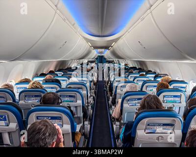 Passengers seated in rows inside a full WestJet airplane cabin during flight, viewed from the aisle looking forward. Stock Photo