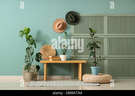 Wooden bench, pouf, folding screen and houseplants near green wall in interior of modern hall Stock Photo