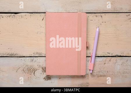 Composition with pink notebook and pen on beige wooden background, closeup Stock Photo