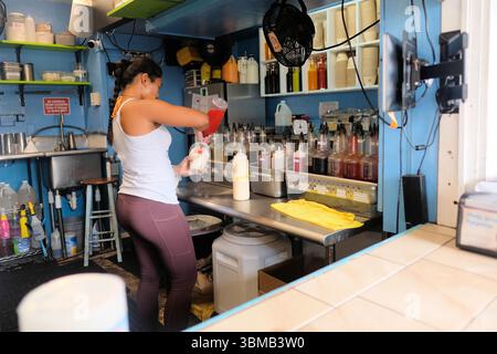 Worker at Jojo's Shave Ice in the Ching Young Village Shopping Center in Hanalei, Kauai, Hawaii, pouring fruit flavored syrup on shaved ice cup. Stock Photo