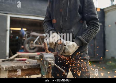 Young Adult Caucasian Man Assembling Custom Bike Using Angle Grinder Outdoors Stock Photo