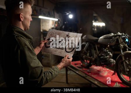 Caucasian Young Adult Man Studying Custom Motorcycle Design Plans in Workshop Stock Photo
