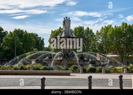 Monumental stone fountain with classical sculptures and multiple water jets, located in a tree-lined square in Aix en Provence. Stock Photo