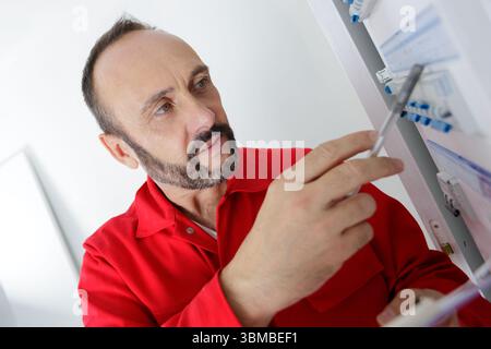 male technician holding clipboard while examining fusebox Stock Photo