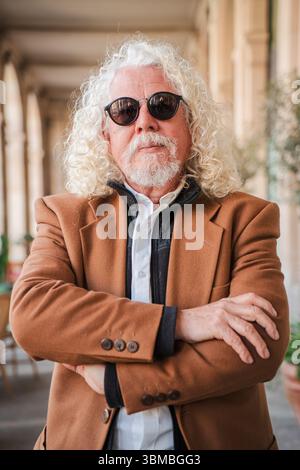 A mature male with curly hair and sunglasses confidently crossing his arms, projecting a sense of strength and seriousness. This portrait captures the Stock Photo