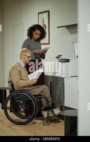 Caucasian Man with Disability and Black Woman Reviewing Documents at Printer Stock Photo
