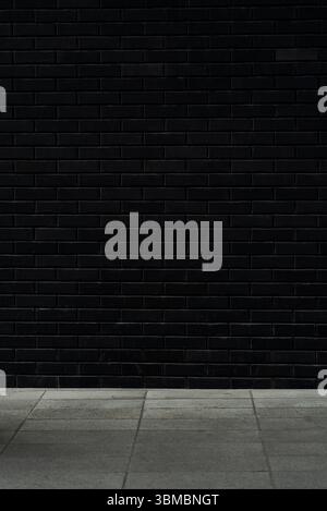 Minimalist urban backdrop: matte black brick wall with empty tiled pavement Stock Photo