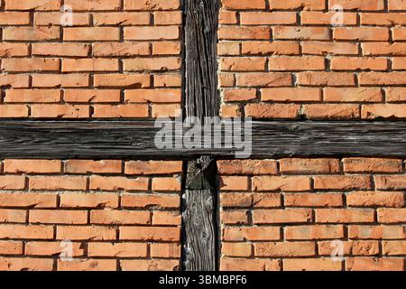 Orange-red brick wall features two intersecting weathered wooden beams forming a cross pattern, highlighting traditional half-timbered construction Stock Photo