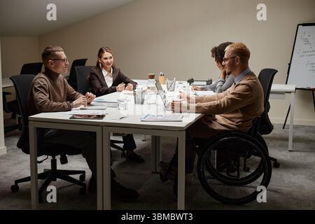 Diverse Young Adults Collaborating in Office Meeting with Man with Disability Stock Photo
