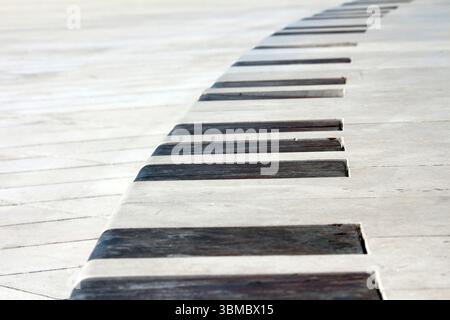 Curved concrete bench with evenly spaced dark wooden slats set into white pavement, forming a repeating geometric pattern in a sunlit urban plaza Stock Photo