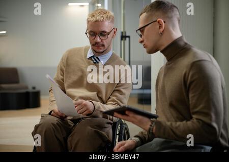 Caucasian Young Adult Men Discussing Documents and Using Digital Tablet Indoors Stock Photo