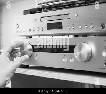Paris, France - Apr 22, 2025: A woman hand is seen turning the large volume knob on a Onkyo P-3000R pre-amplifier, with an Onkyo SACD player above it Stock Photo