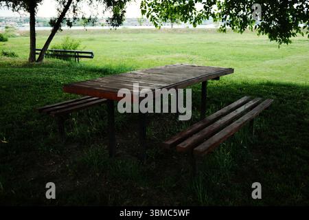 Wooden picnic table and benches under tree shade in a public park. Small Serbian town Stock Photo